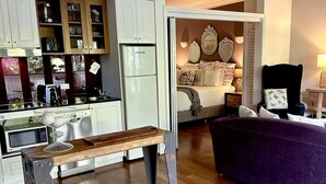 Eine moderne Küche mit weißen Schränken, einem Holzespeisetisch und einem violetten Sofa im Wohnbereich.