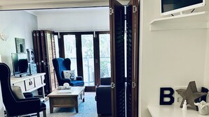 Ein Hotelzimmer mit Bett, Schreibtisch mit Fernseher, Sessel, Sofa und Blick ins Freie.
