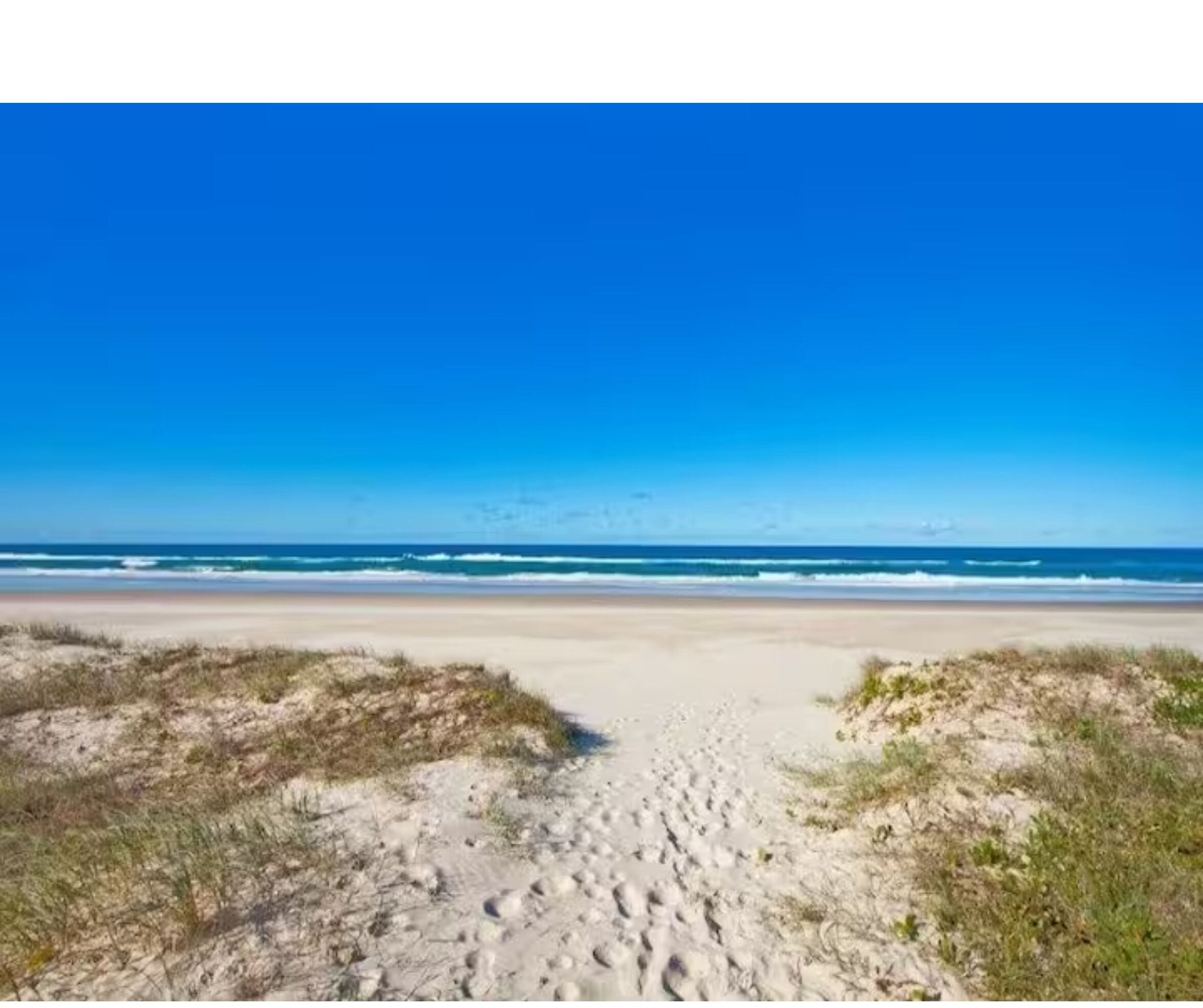 A beach with a clear sky and waves in the background.