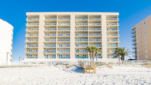 A multi-story hotel with balconies, a sandy beach in front, and palm trees. - Surfside Shores II 2204 Directly On The Gulf Of America (Gulf Shores)