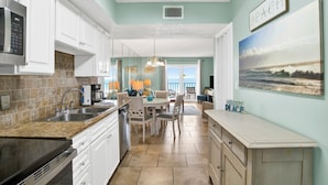 A kitchen with a granite countertop, stainless steel appliances, and a dining area with a table and chairs. - Surfside Shores II 2204 Directly On The Gulf Of America (Gulf Shores)