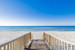 A wooden boardwalk leading to a sandy beach with clear blue water.