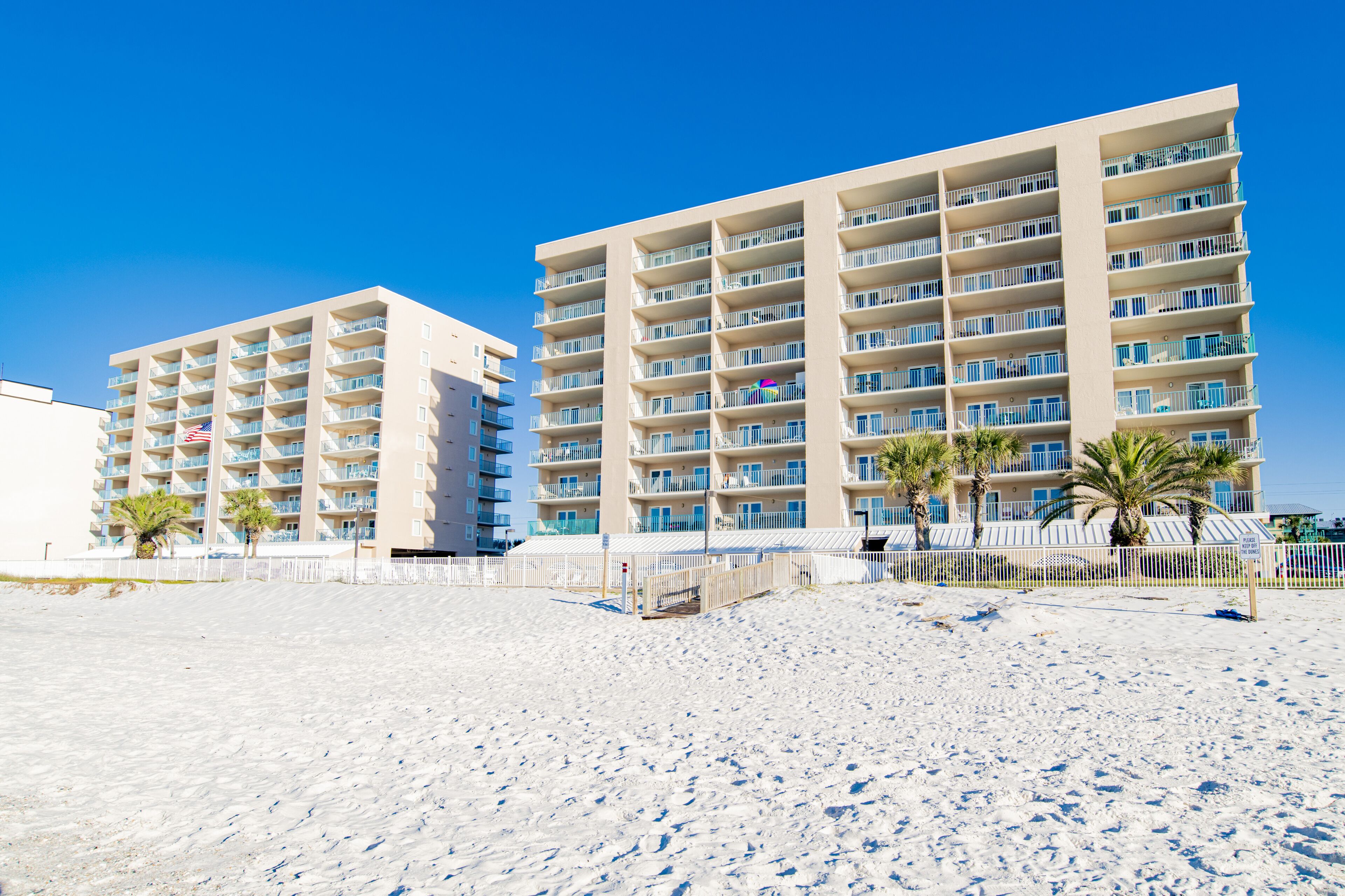 A beachfront hotel with multiple floors, balconies, and a sandy beach in the foreground.