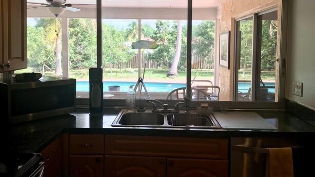 Una cocina con un amplio ventanal que da a una piscina y abundante vegetación.