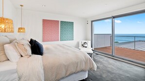 A modern bedroom with a large bed, a balcony with a view of the sea, and two abstract wall art pieces. - Azure - Absolute Beachfront Luxury, Wifi, Spa (Lorne)
