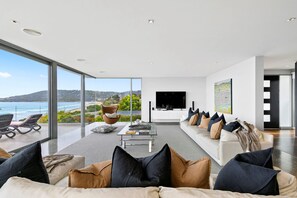 Un salon moderne doté d’une grande fenêtre offrant une vue panoramique, d’un téléviseur à écran plat fixé au mur et d’un espace détente avec plusieurs canapés et fauteuils.