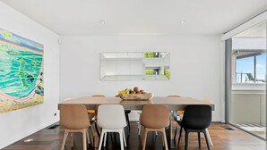 A modern dining area with a large table, six chairs, and a fruit bowl. - Azure - Absolute Beachfront Luxury, Wifi, Spa (Lorne)