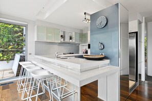 A modern kitchen with a central island, bar stools, a built-in oven, and a clock on the wall. - Azure - Absolute Beachfront Luxury, Wifi, Spa (Lorne)