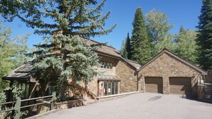 A stone building with a large tree in front, a covered porch, and two garage doors. - Large 6 Bedroom Home- Ski-in / Ski-out Access (202983-2164) (Snowmass Village)