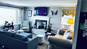 A living room with a fireplace, a sofa, a chair, and a television. -  Beautiful Waterfront Home (Misquamicut)