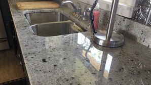 A kitchen with granite countertops, stainless steel sinks, and a wooden cutting board. -  Beautiful Waterfront Home (Misquamicut)
