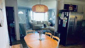 A dining area with a wooden table and chairs, a hanging light fixture, and a refrigerator in the background. -  Beautiful Waterfront Home (Misquamicut)