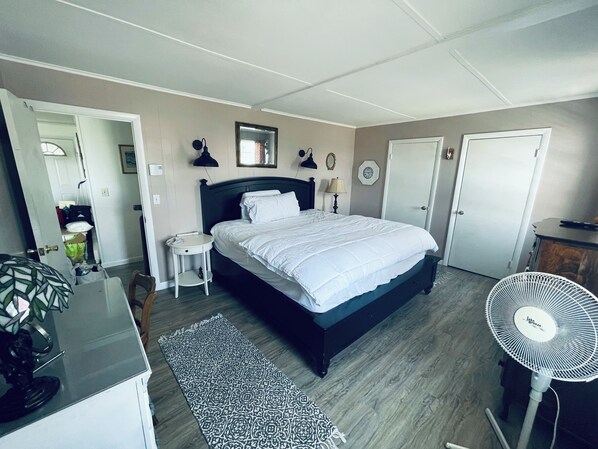 A bedroom with a bed, bedside table, lamp, and a standing fan. - Beautiful Waterfront Home (Misquamicut)