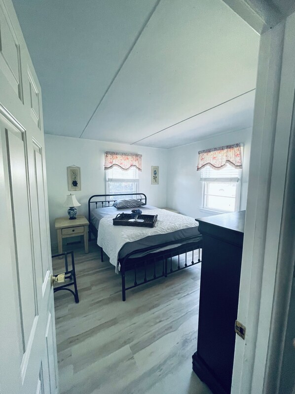 Une chambre à coucher comprenant un lit, des tables de chevet, une commode, une coiffeuse et deux fenêtres avec des rideaux.