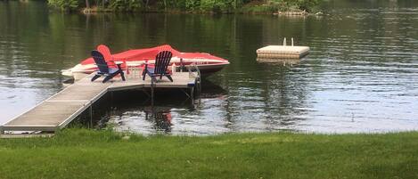 Un muelle con un bote y sillas, rodeado de agua y vegetación.