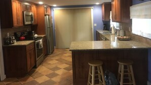 A compact kitchen with wooden cabinets, a microwave, a refrigerator, a stove, and a sink. There are two stools at the counter. - Lake Rescue Vacation Home- Pets Welcome-Okemo and Killington close!!! (Ludlow)