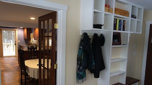 A dining area with a wooden table and chairs, a bookshelf with books and a sign, and a coat rack with jackets. - Lake Rescue Vacation Home- Pets Welcome-Okemo and Killington close!!! (Ludlow)