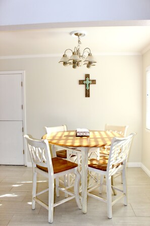 Un coin repas avec une table ronde et des chaises blanches, un lustre et une croix en bois accrochée au mur.
