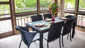 A covered outdoor dining area with wicker chairs and a glass table set for four. - Beachfront | Beachside Private Pool | Immaculately Kept | Private Dive Resort (Roatan)