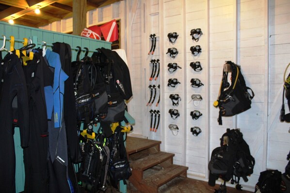 A room with a wooden staircase, a wall with various helmets and helmets, and several bags and backpacks.
