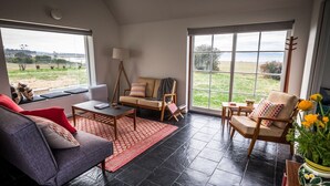 Ein geräumiges Wohnzimmer mit Sofa, Sessel und Couchtisch, große Fenster mit Blick ins Freie.