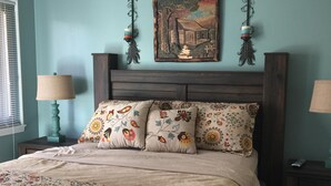 A bedroom with a bed, two nightstands, a window, and a wall painting.