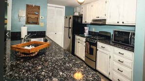 A kitchen with white cabinets, a black refrigerator, a stove, a microwave, and a granite countertop.