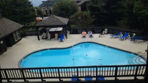 A swimming pool with lounge chairs and a covered seating area, surrounded by buildings and trees, with mountains in the background.