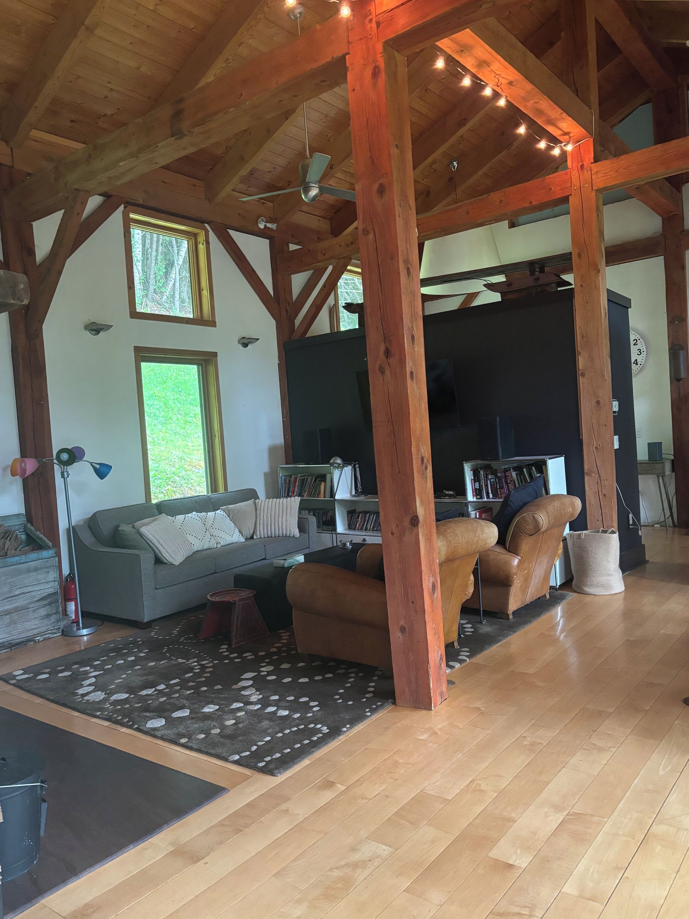 A spacious living room with wooden beams, a sofa, two armchairs, a coffee table, and a bookshelf.