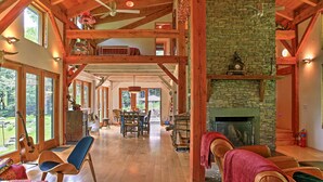 A spacious interior with a high ceiling, wooden beams, a fireplace, and a dining area with a view of the outdoors. - House Belleayre peaceful spring water swimming pond (Fleischmanns)