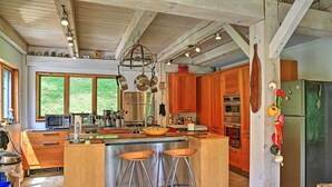 A modern kitchen with wooden cabinets, a large island with stools, stainless steel appliances, and a hanging pot rack. - House Belleayre peaceful spring water swimming pond (Fleischmanns)