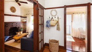 A living room with a fireplace, a sofa, a coffee table, and a ceiling fan. There is a wicker basket on the floor and a white chair in the background. - Jetty Beach House (Coffs Harbour)