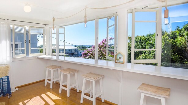 A bright room with large windows, wooden floor, and white furniture. - Jetty Beach House (Coffs Harbour)