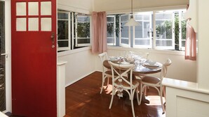 A dining area with a round table set for four, white chairs, and a red door. - Jetty Beach House (Coffs Harbour)