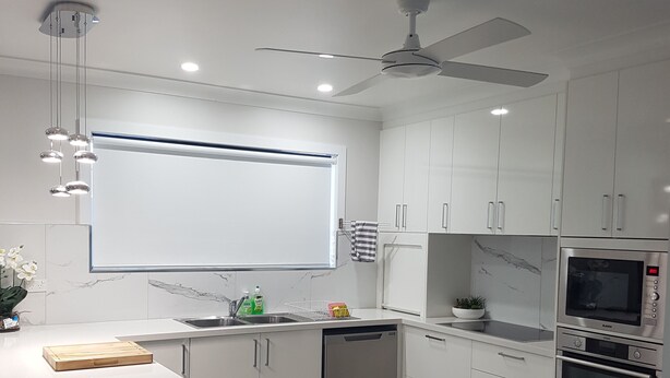 A modern kitchen with white cabinets, a built-in oven, and a ceiling fan.