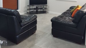 A modern living room with a flat-screen TV, two leather sofas, and a ceiling fan.