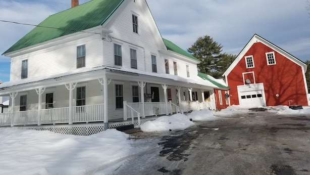 Une maison blanche à deux étages, avec un toit vert et une grange rouge.