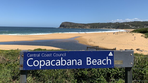 Señal de playa para la Playa Copacabana, con vista al océano y una colina distante.