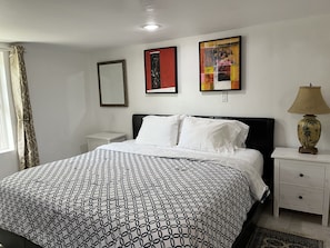 Quarto com cama, mesas de cabeceira brancas, abajur e duas obras de arte emolduradas na parede.
