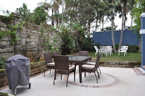 Um pátio externo com mesa, cadeiras, churrasqueira e uma parede de pedra.