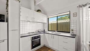 Una cocina moderna con armarios blancos, horno empotrado, estufa a gas y ventana con vistas al exterior.