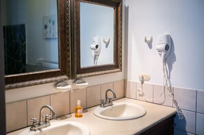 A bathroom with two sinks, a mirror, and a hairdryer on the wall.
