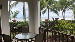 Un balcon avec une table ronde et quatre chaises, donnant sur une plage bordée de palmiers et sur l’océan.