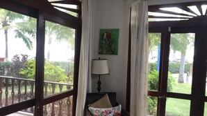 Une pièce donnant sur un jardin, une chaise avec un coussin à motifs floraux, une lampe et un tableau accroché au mur.