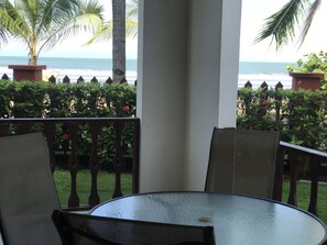 A round glass table with two chairs, a white pillar, and a view of the ocean.