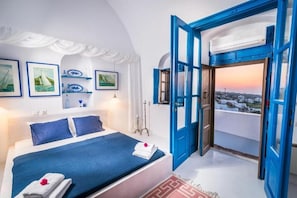 Ein Schlafzimmer mit einem Bett, Blick durch eine offene Tür und gerahmten Bildern an der Wand.