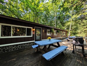 A wooden deck with picnic tables and a barbecue grill, surrounded by trees. - Amenities & Resort Access Included, Cabin 3 (Phelps)