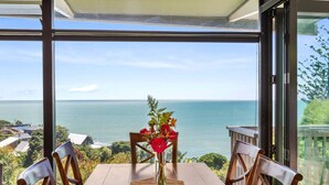 A dining area with a table and chairs, a vase with flowers, and a view of the sea. - G SPOT (upper level) WITH SPA (Raglan)