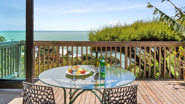 A glass table with a meal and drinks on a wooden deck with a view of the ocean. - G SPOT (upper level) WITH SPA (Raglan)