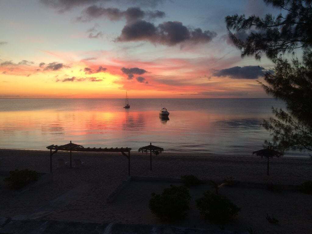 A beach scene with a sunset, calm sea, and a few boats.